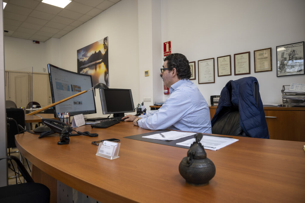 Un hombre con camisa azul sentado en un escritorio mirando la pantalla de un ordenador.